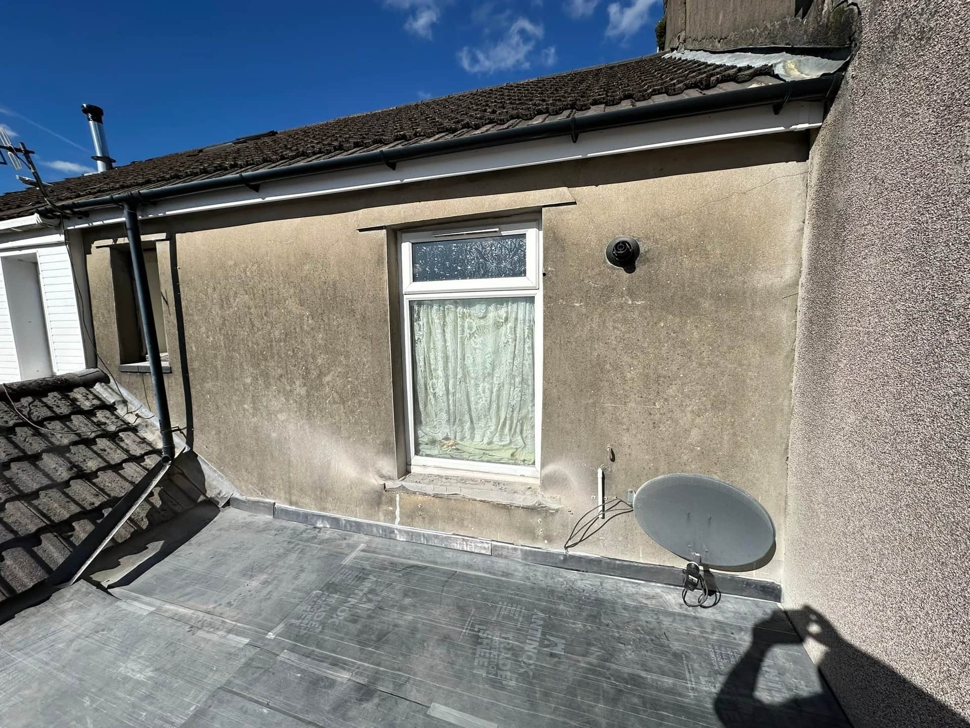 Before: rear elevation of a Rhondda house, tired render replaced with crisp white cladding and a new gutter line