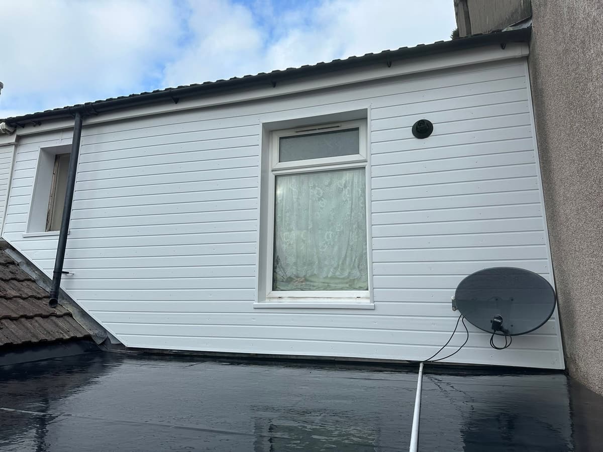 After: rear elevation of a Rhondda house, tired render replaced with crisp white cladding and a new gutter line