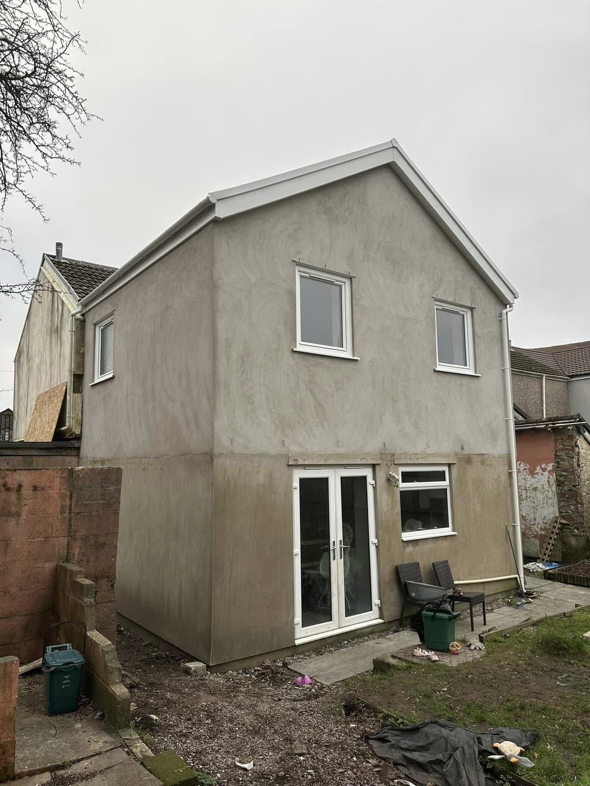After: extension under construction with roof tiles going on behind scaffolding, then the finished two-storey rendered extension with French doors